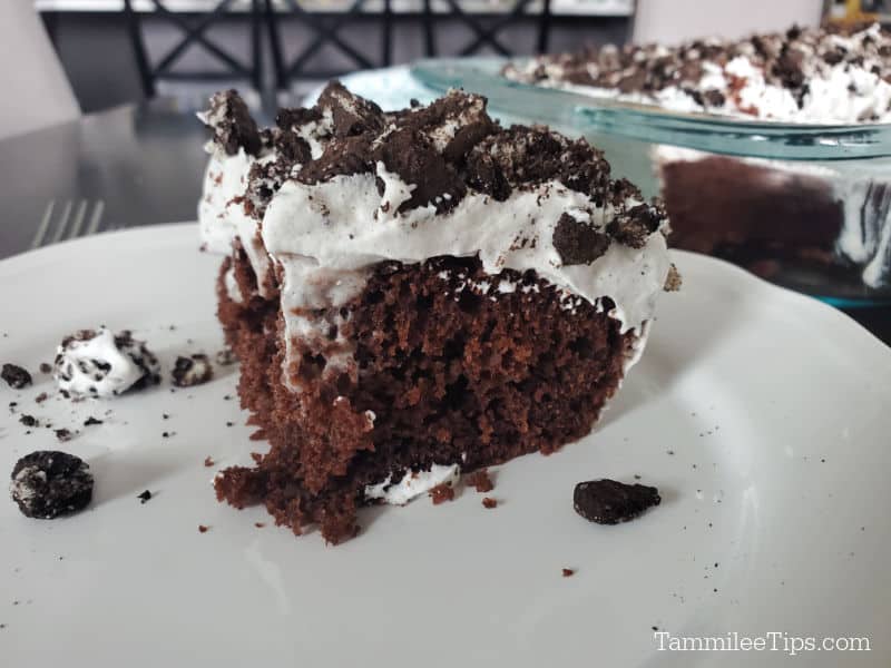 Square piece of Oreo Poke Cake on a white plate with the baking dish in the background. 