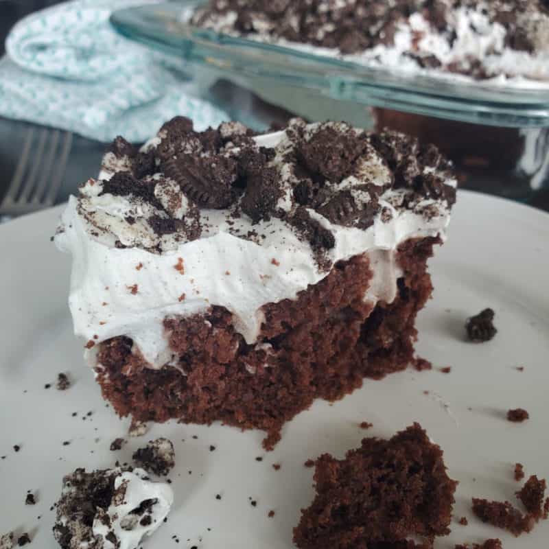 Slice of Oreo Poke Cake on a white plate next to the cake dish