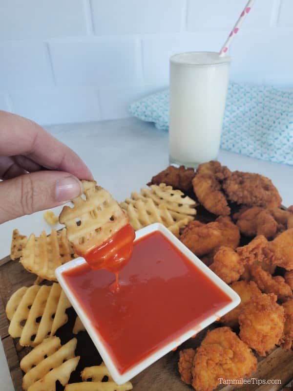 French fry dipping into Polynesian Sauce Chick Fil A copy cat with additional French fries and chicken surrounding the bowl 