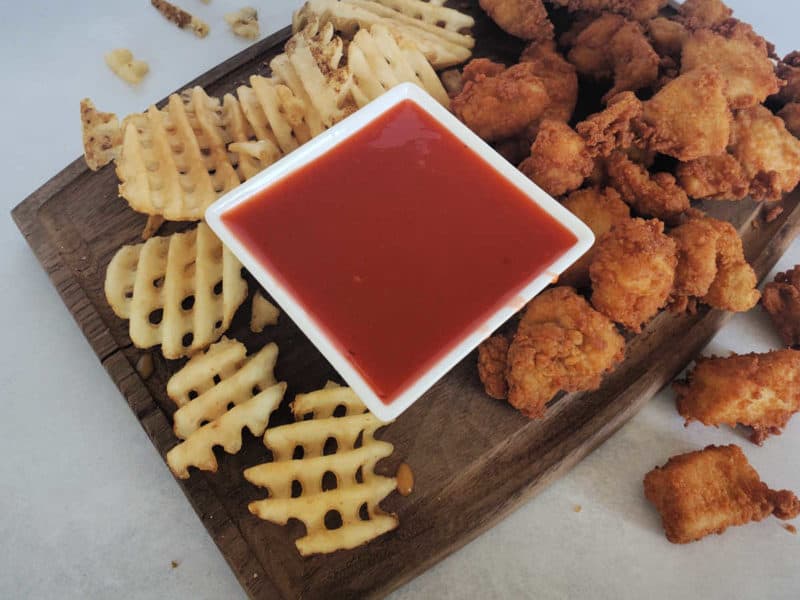 copycat polynesian sauce in a square bowl on a cutting board with french fries and chicken 