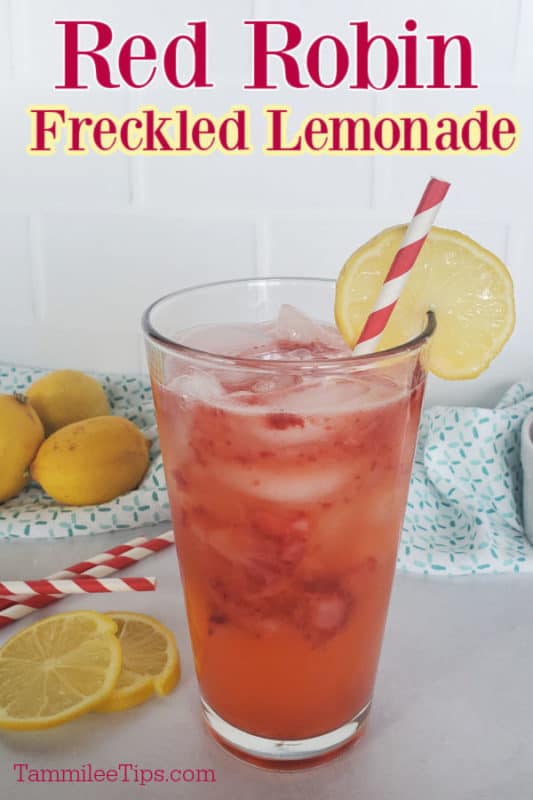 Red Robin Freckled Lemonade over a glass with strawberry lemonade garnished with a lemon wheel. Lemons and a cloth towel in the background. 