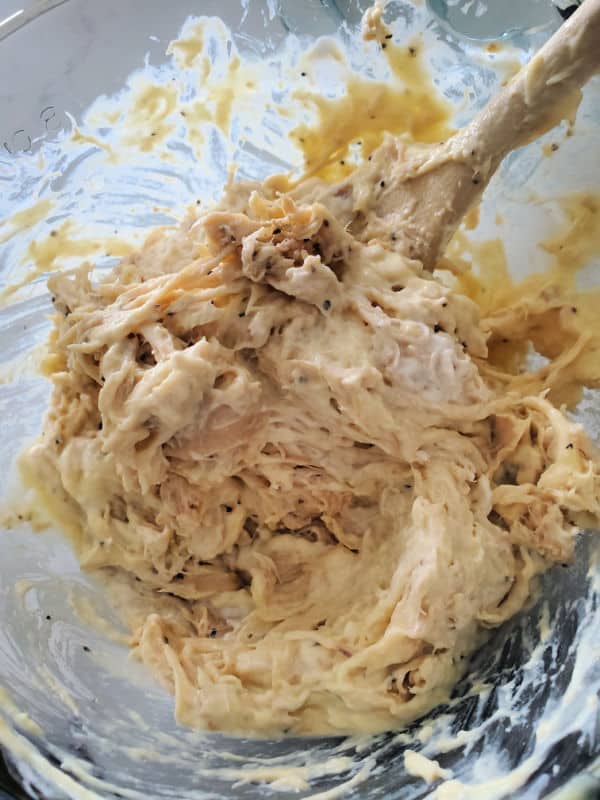 shredded chicken sour cream mixture in a glass bowl with a wooden spoon