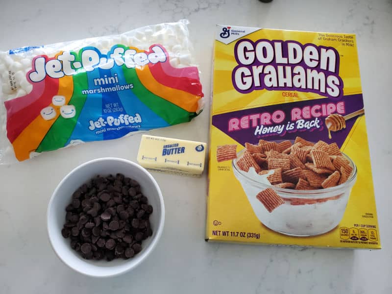 Mini Marshmallows, bowl of chocolate chips, stick of butter, and Golden Grahams cereal box on a white counter. 