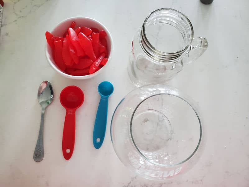 Swedish Fish Candy in a white bowl, mason jar glass, fish bowl, spoon, measuring tools on a white counter