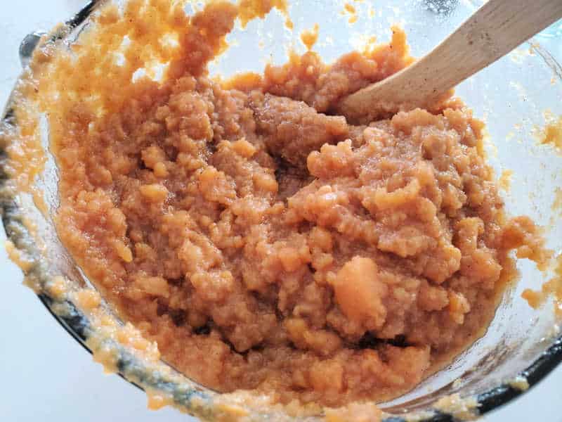 mashed sweet potatoes in a glass bowl with a wooden spoon