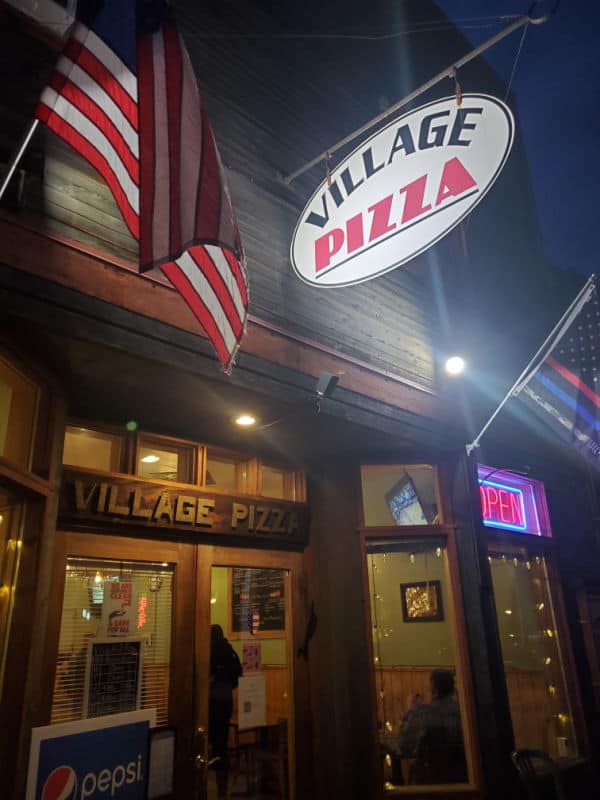 Village Pizza sign, American flag, and restaurant entrance in Roslyn. 