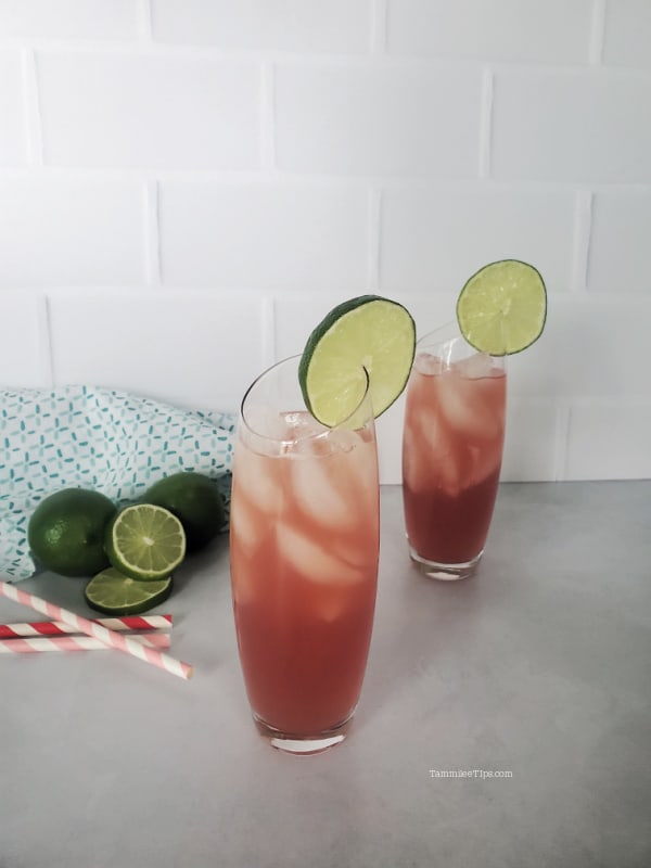 Bay Breeze Cocktail with lime wheels, limes and paper straws next to them. 