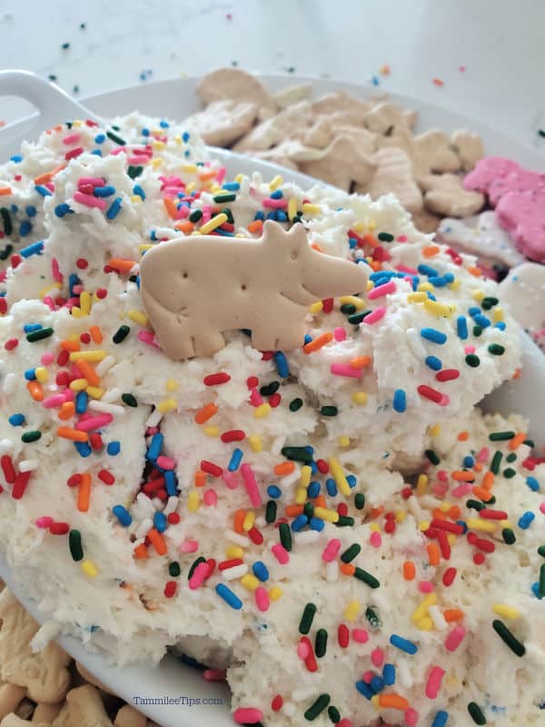 funfetti dip in a white bowl with sprinkles and an animal cracker as a garnish. 