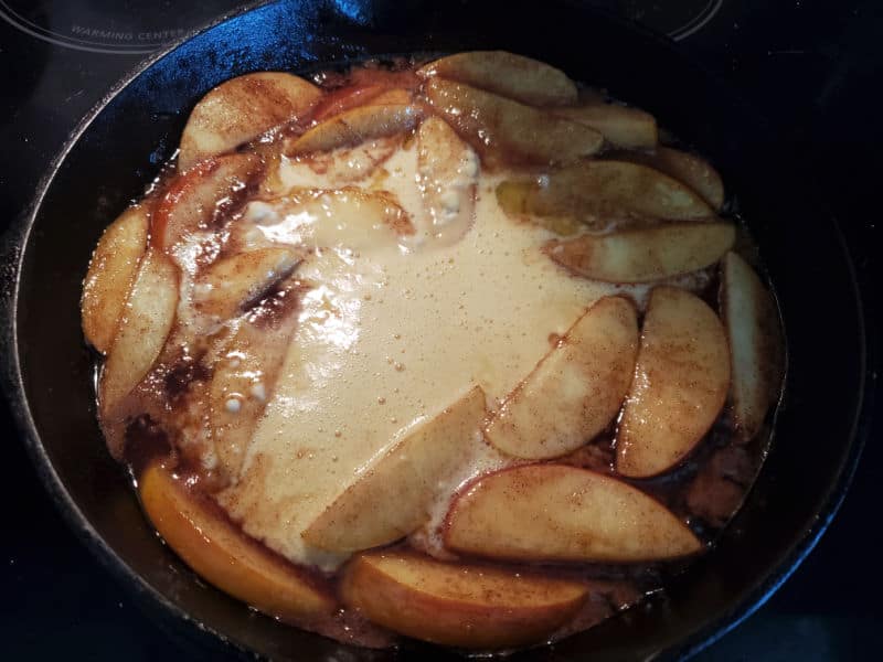 German apple pancake batter over fried apples in a cast iron skillet