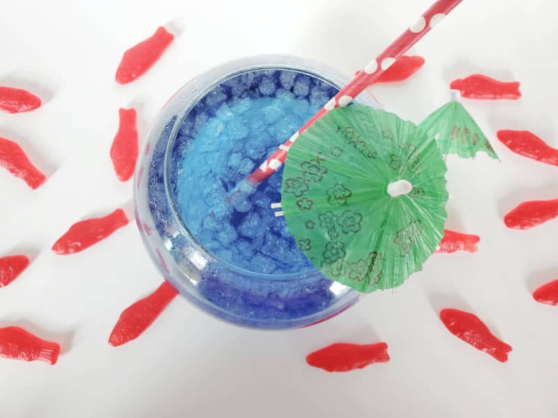 Blue Sonic Ocean Water drink in a fish bowl with a green umbrella and red straw surrounded by Swedish Fish Candies