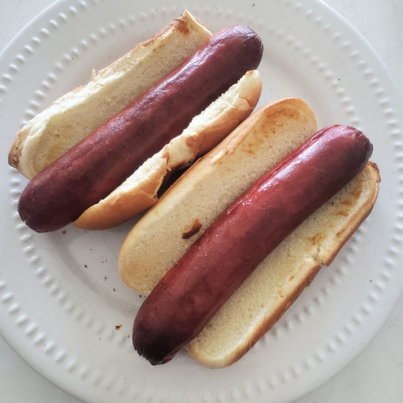 two air fried hot dogs on toasted buns on a white plate