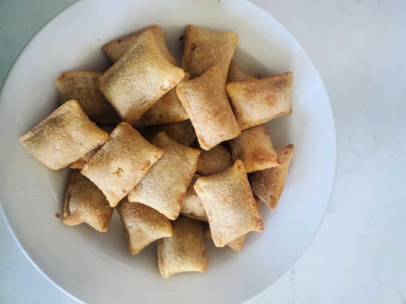 Air fryer pizza rolls in a white bowl on a white counter. 