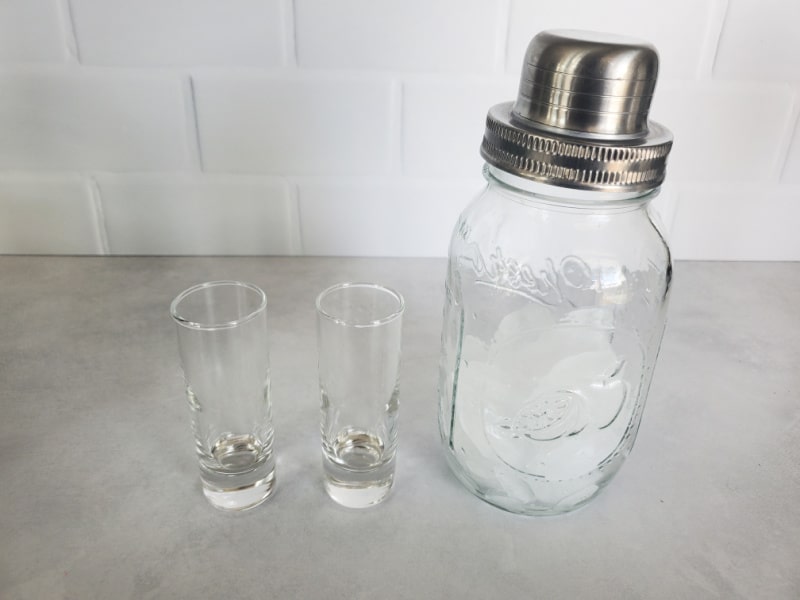 Two clear glass shot glasses with a mason jar cocktail shaker 