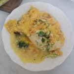 broccoli cheddar chicken on a white plate next to a wooden cutting board