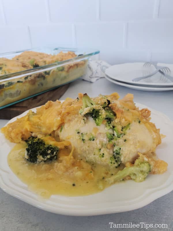chicken breast covered in broccoli, ritz crackers, and cheese sauce on a white plate next to a glass baking dish. 