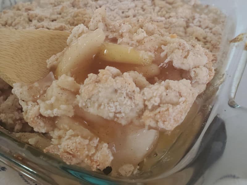 Wooden spoon scooping apple cobbler out of a baking dish. 