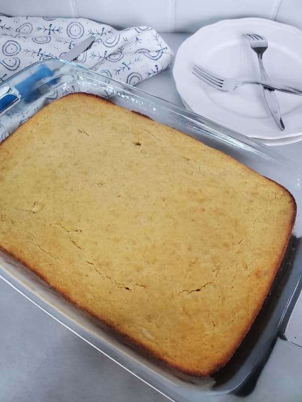 Cornbread in a glass baking dish next to a stack of white plates with forks sitting on the plates