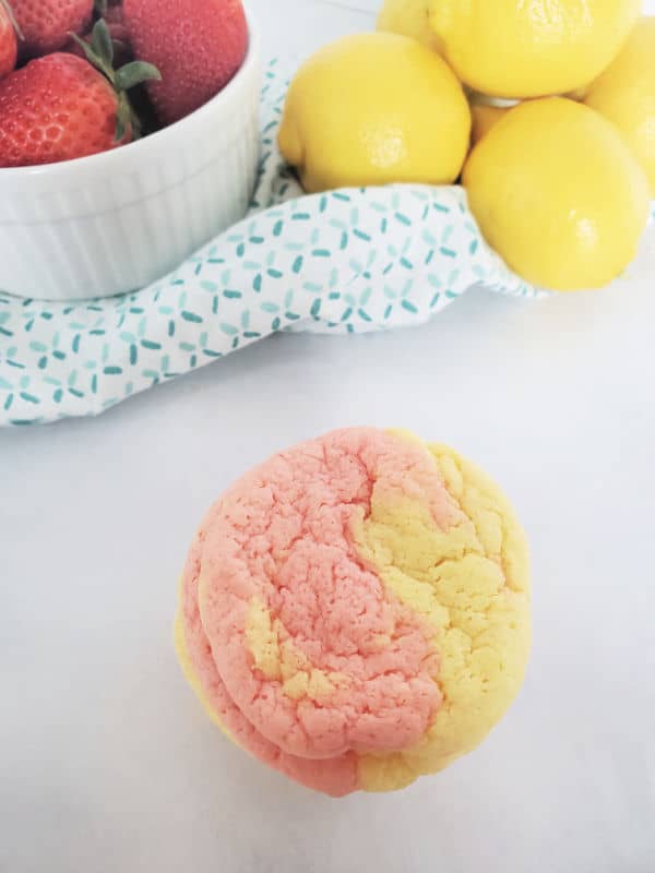 stack of pink and yellow strawberry lemonade cookies next to a bowl of strawberries and lemons. 