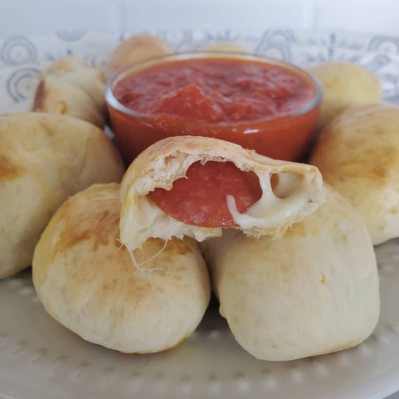 split open pepperoni roll sitting on top of other rolls next to a bowl of marinara sauce
