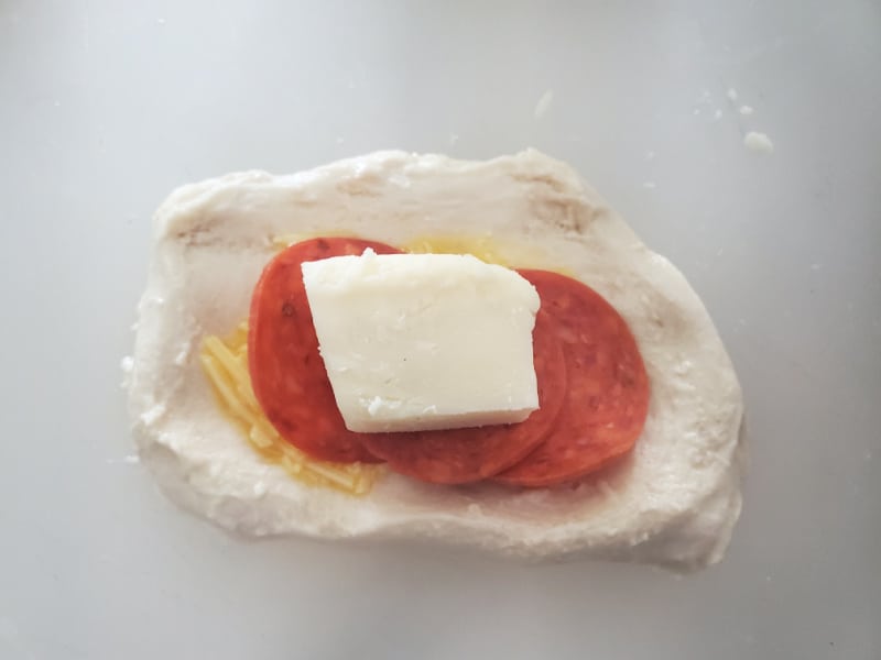 piece of mozzarella on top of pepperoni slices on a circle of bread dough