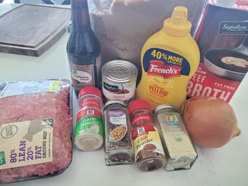 ground beef, garlic powder, chili powder, onion powder, onion, mustard, tomato sauce, brown sugar, and beef broth on a white counter 