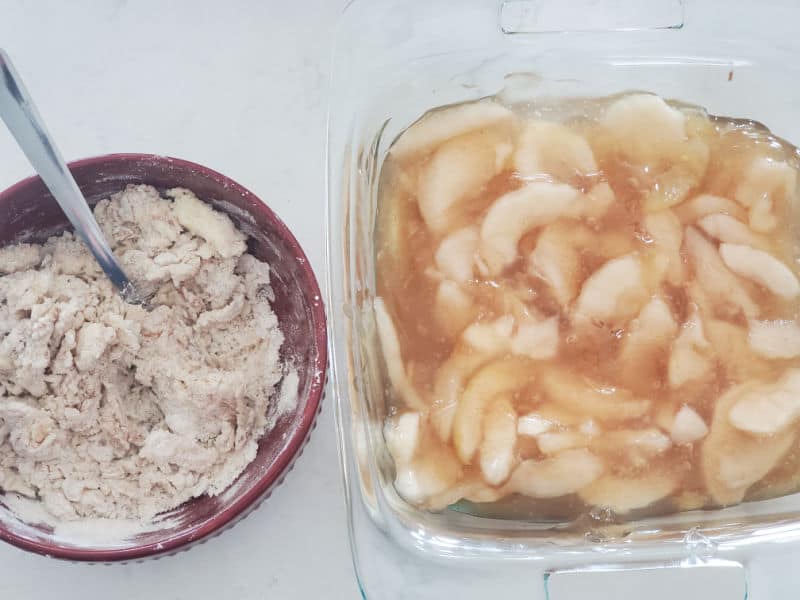 Bowl with cobbler mix and a spoon next to a glass baking dish with apples