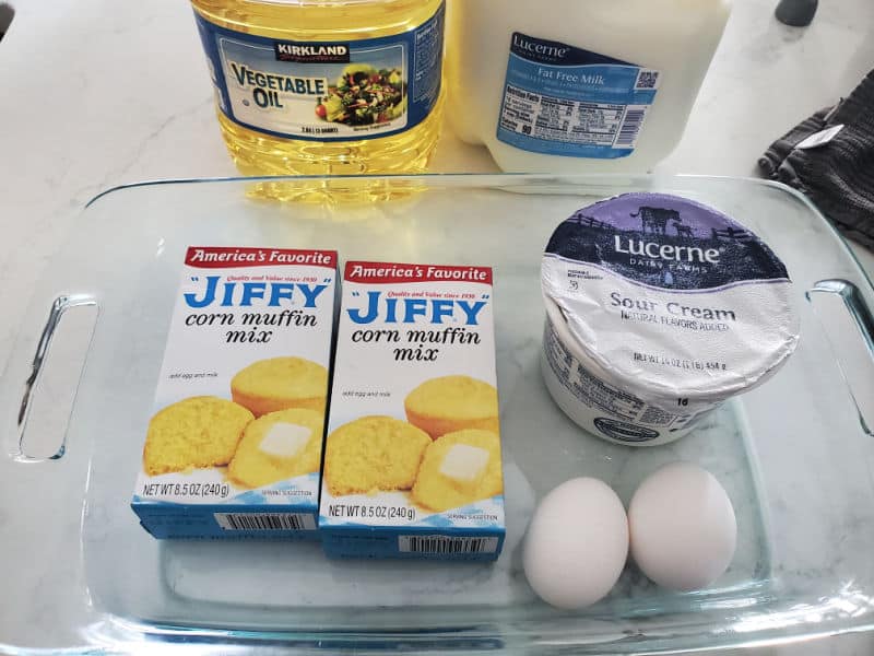 Jiffy Corn Muffin mix, sour cream, and two eggs in a glass baking dish next to vegetable oil and milk 