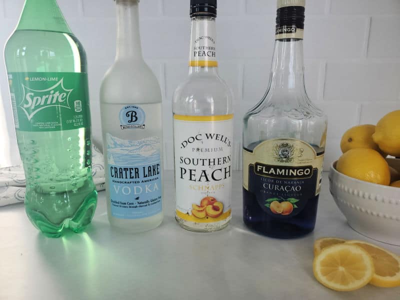 Sprite, Vodka, Peach Schnapps, Blue curacao bottles next to a bowl of lemons
