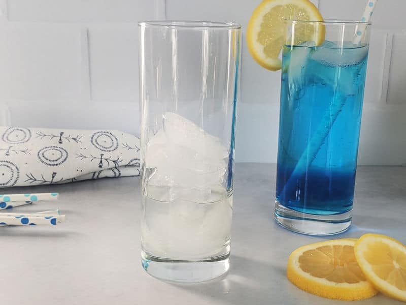 Glass with ice next to a glass with blue drink and a lemon wheel