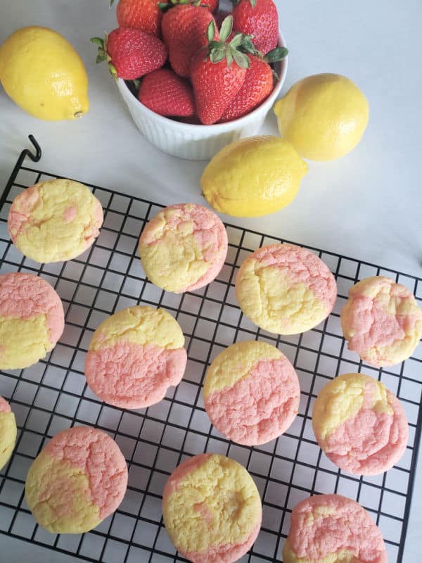 strawberry lemonade cookies on a wire rack next to a bowl of strawberries and lemons. 