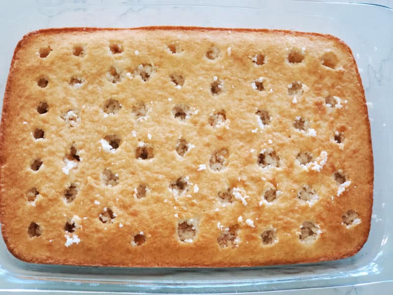 White cake with holes poked in the top of it in a baking dish