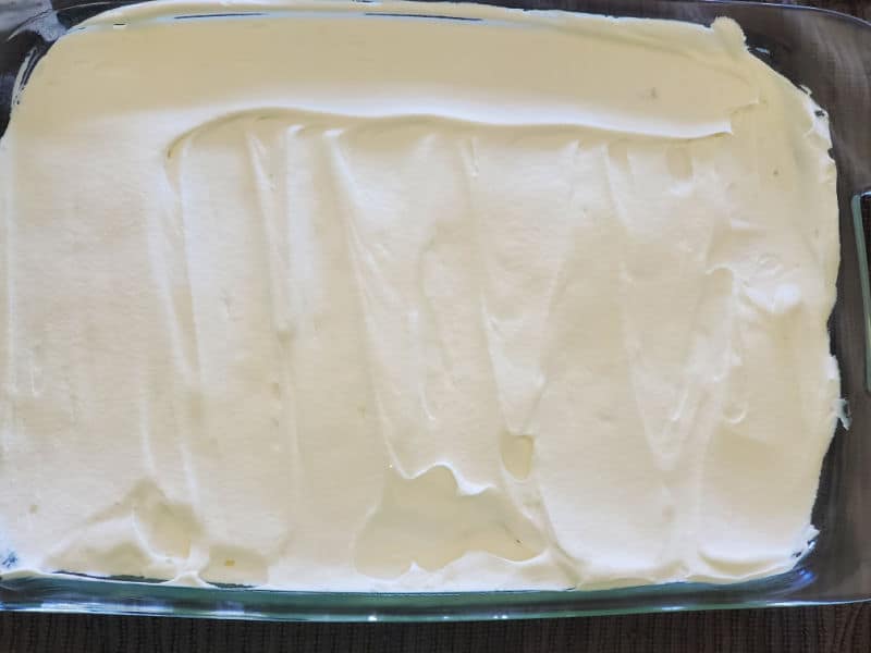 Whip cream spread evenly across a cake in the baking dish