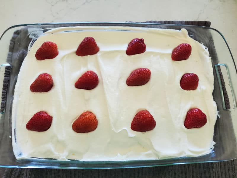 Cut strawberries lined up on whipped topping in a baking dish