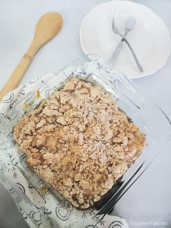 Bisquick apple cobbler in a baking dish next to a wooden spoon, white plate with forks. 