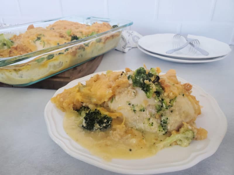 broccoli cheddar chicken casserole on a white plate next to the baking dish