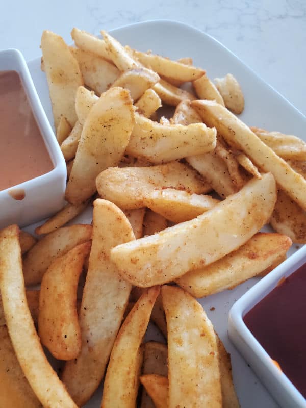 Air fryer French fries on a white plate with dipping sauces. 