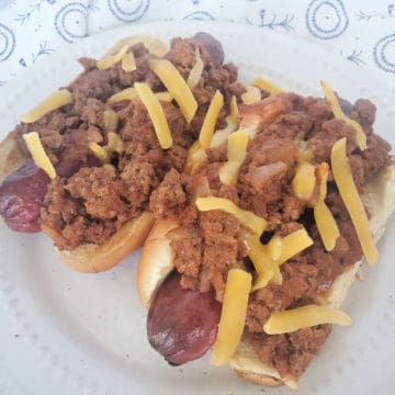 two chili dogs covered in homemade hot dog chili on a white plate