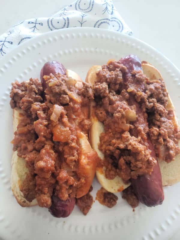 two chili dogs with homemade hot dog chili over them on a white plate
