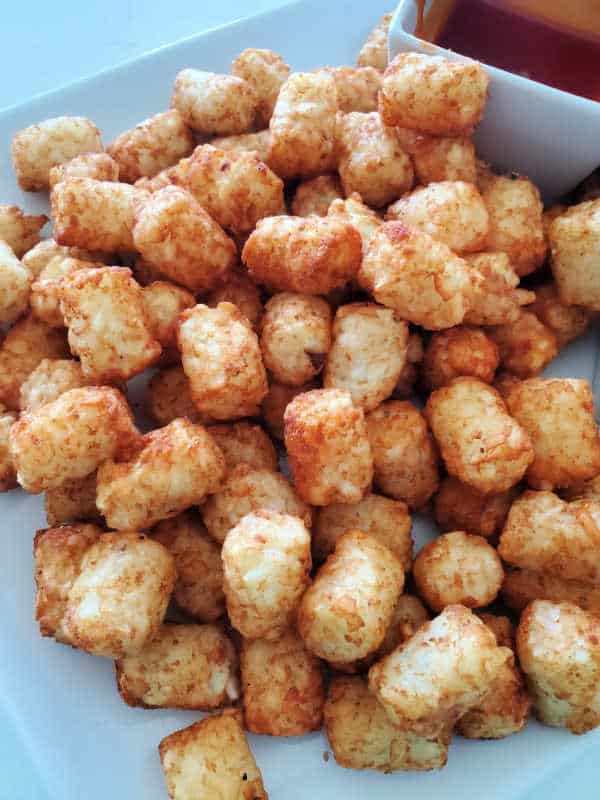 Air fryer tater tots on a white plate with dipping sauce. 