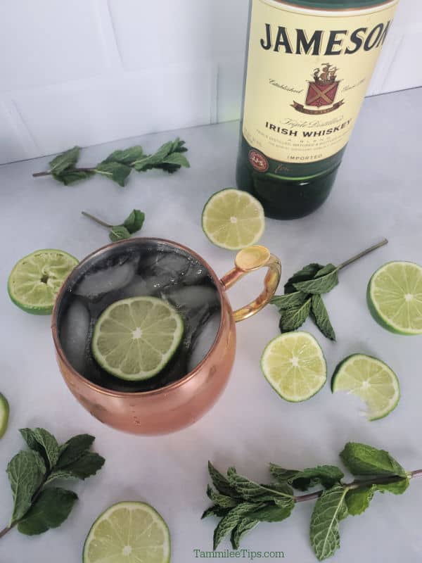 Irish Mule in a Copper Mug next to a bottle of Jameson Whisky and lime wheels and mint sprigs