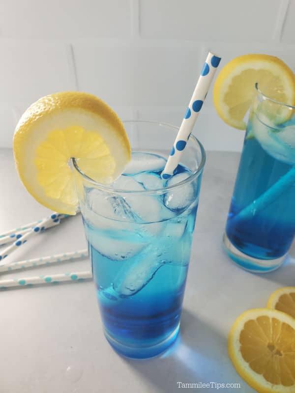 Looking down on a blue drink with a lemon wheel garnish and paper straw