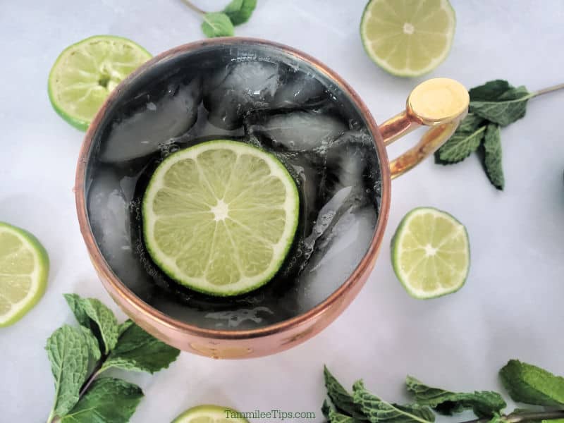 Looking down into an Irish Mule Cocktail in a copper mule mug with a lime wheel garnish surrounded by limes and mint sprigs