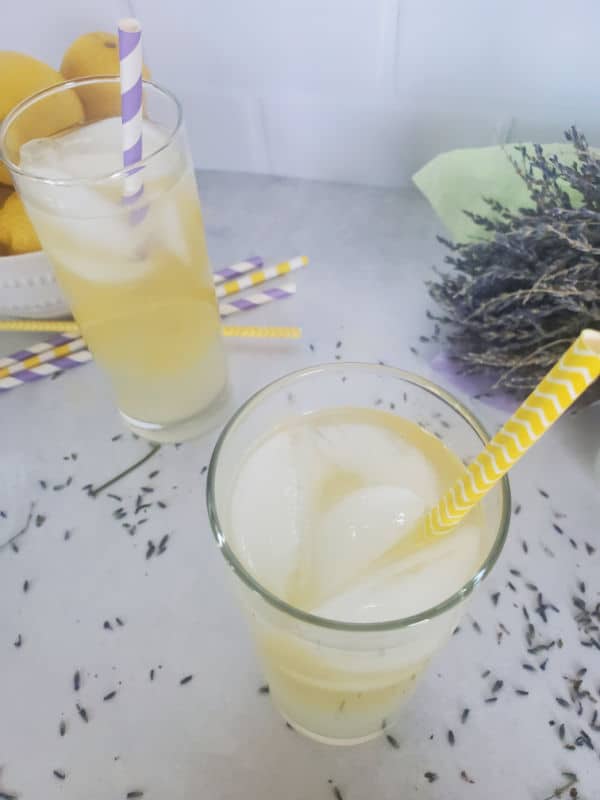 Lavender lemonade cocktails in tall glasses with paper straws next to a bundle of lavender