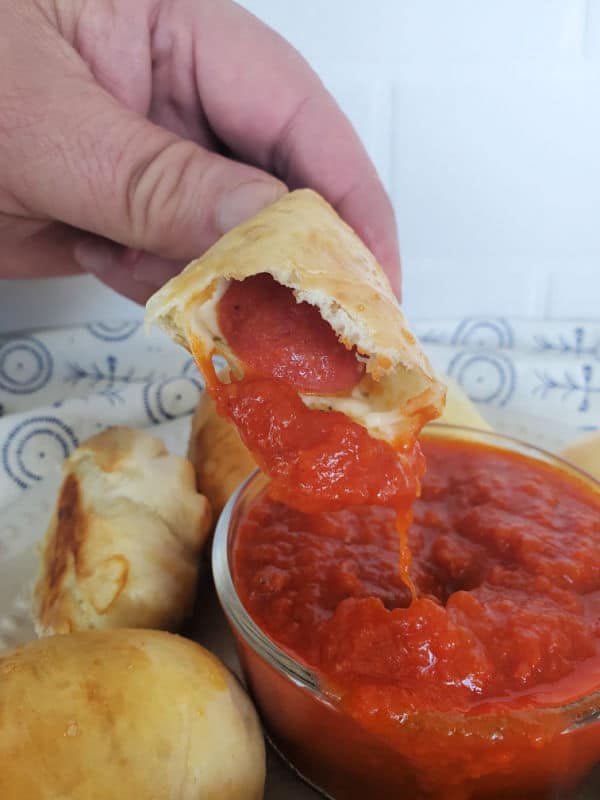 hand holding a pepperoni roll dipping into a bowl of marinara sauce