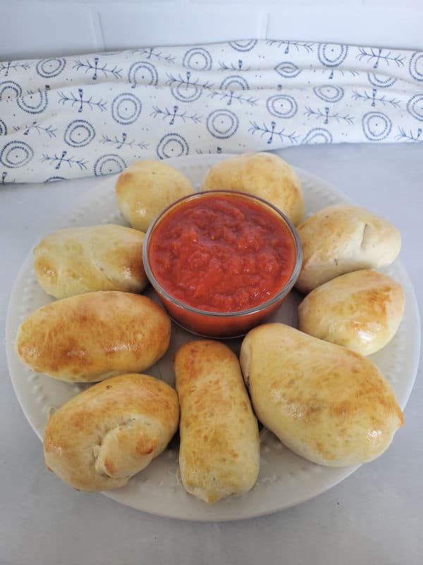 pepperoni rolls on a white plate next to a bowl of marinara sauce
