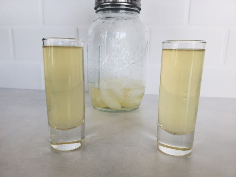 Two Green Tea Shots in clear glass shot glasses with a mason jar cocktail shaker behind them. 