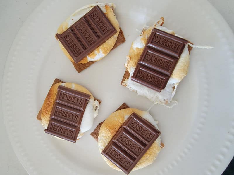 graham crackers with squished marshmallows topped with Hershey's chocolate on a white plate