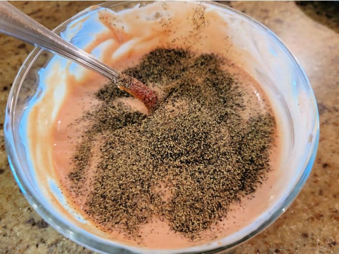 Pepper on top of a pink sauce with a spoon in a glass bowl