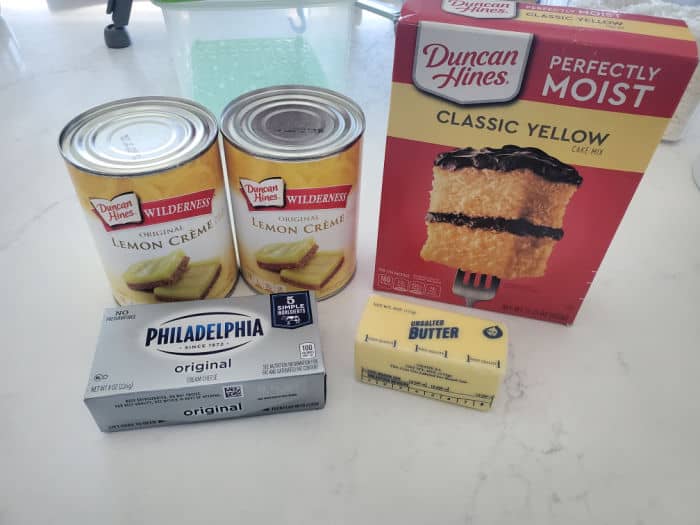 lemon creme cans, cream cheese, butter, and classic yellow cake mix box on a white counter. 