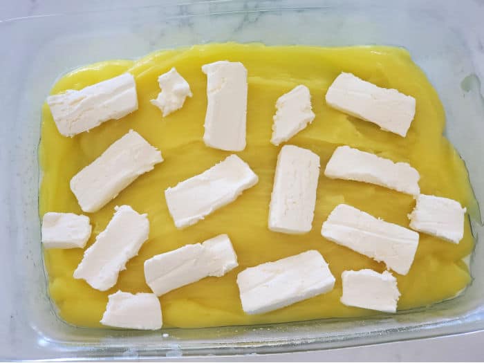 Cream cheese pieces on lemon cream pie filling in a glass baking dish